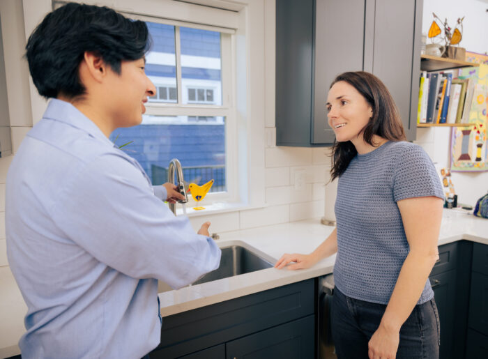 Tacoma plumber running water to test a kitchen faucet while talking with a homeowner about the repair