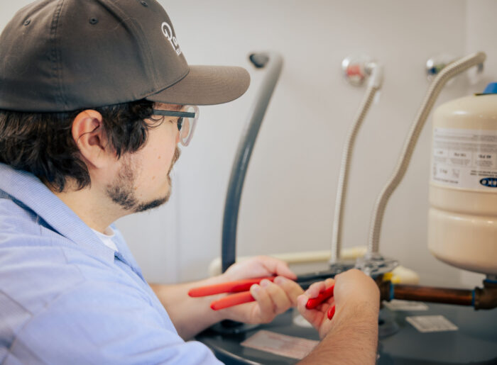 Tacoma plumber installing a water heater, tightening the flexible supply line connections with pliers next to the expansion tank