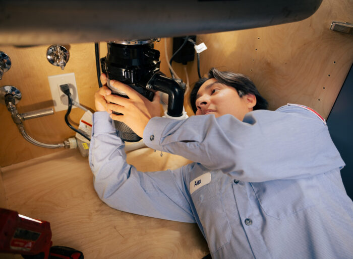 Tacoma plumber lying under a kitchen sink installing a garbage disposal, holding the unit in place while connecting the drain