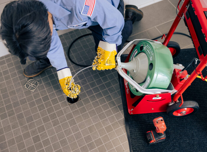 Overhead view of a Tacoma plumber feeding a powered drain auger cable into a floor drain to clear a clog