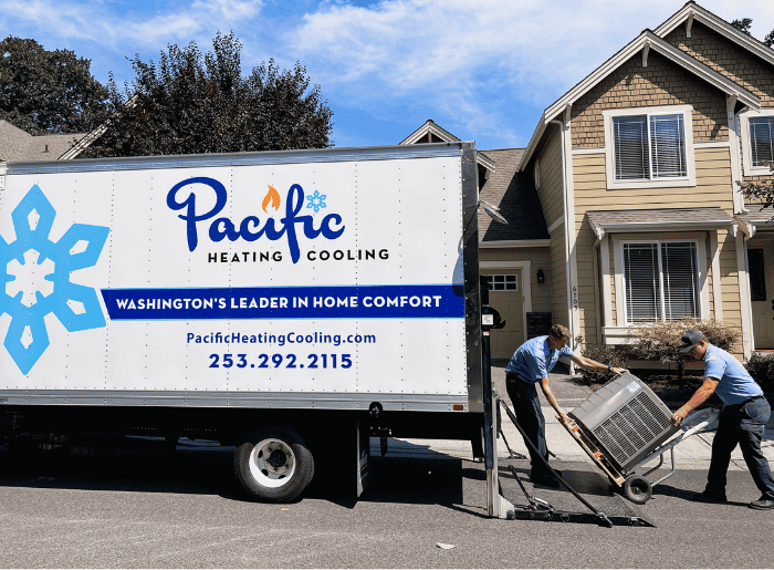 HVAC technicians unloading equipment from a Pacific Heating & Cooling service truck in a residential driveway