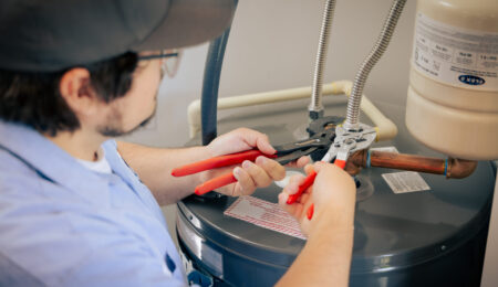 Close-up of a Tacoma plumber using two pairs of pliers to tighten the supply line fittings on top of a water heater