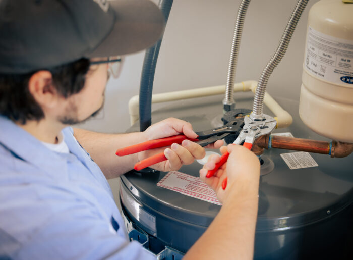 Close-up of a Tacoma plumber using two pairs of pliers to tighten the supply line fittings on top of a water heater