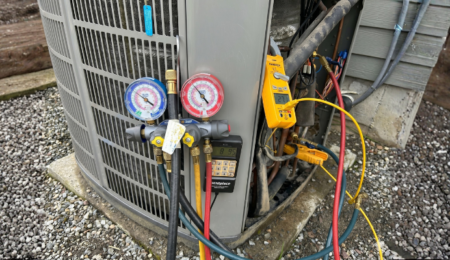 Technician checking AC refrigerant pressure with manifold gauges on outdoor condenser unit in Tacoma