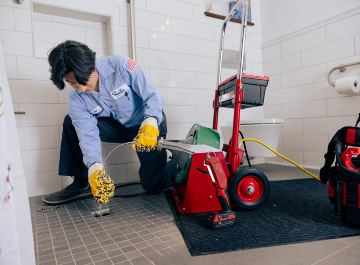 Tacoma plumber feeding a powered drain snake into a bathroom floor drain to clear a clog
