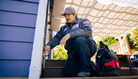 Tacoma plumber kneeling on a patio using pliers to repair an outdoor hose bib faucet on the side of a home