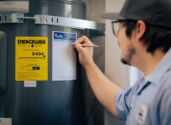 Tacoma plumber writing service details on a maintenance record label attached to an electric water heater tank