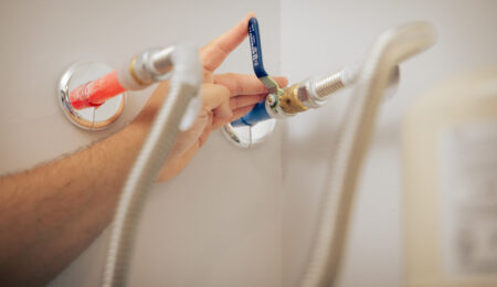 Hand turning a blue lever ball valve to shut off a water supply line