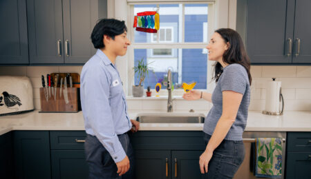 Pacific Heating & Cooling plumber talking with a homeowner at a running kitchen faucet in a Tacoma home