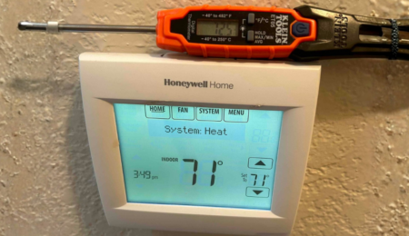 Technician checking thermostat accuracy with a probe thermometer during a no heat repair call