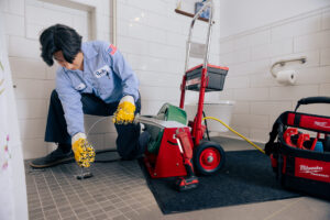 Pacific Heating & Cooling technician clearing a drain clog with a cable machine
